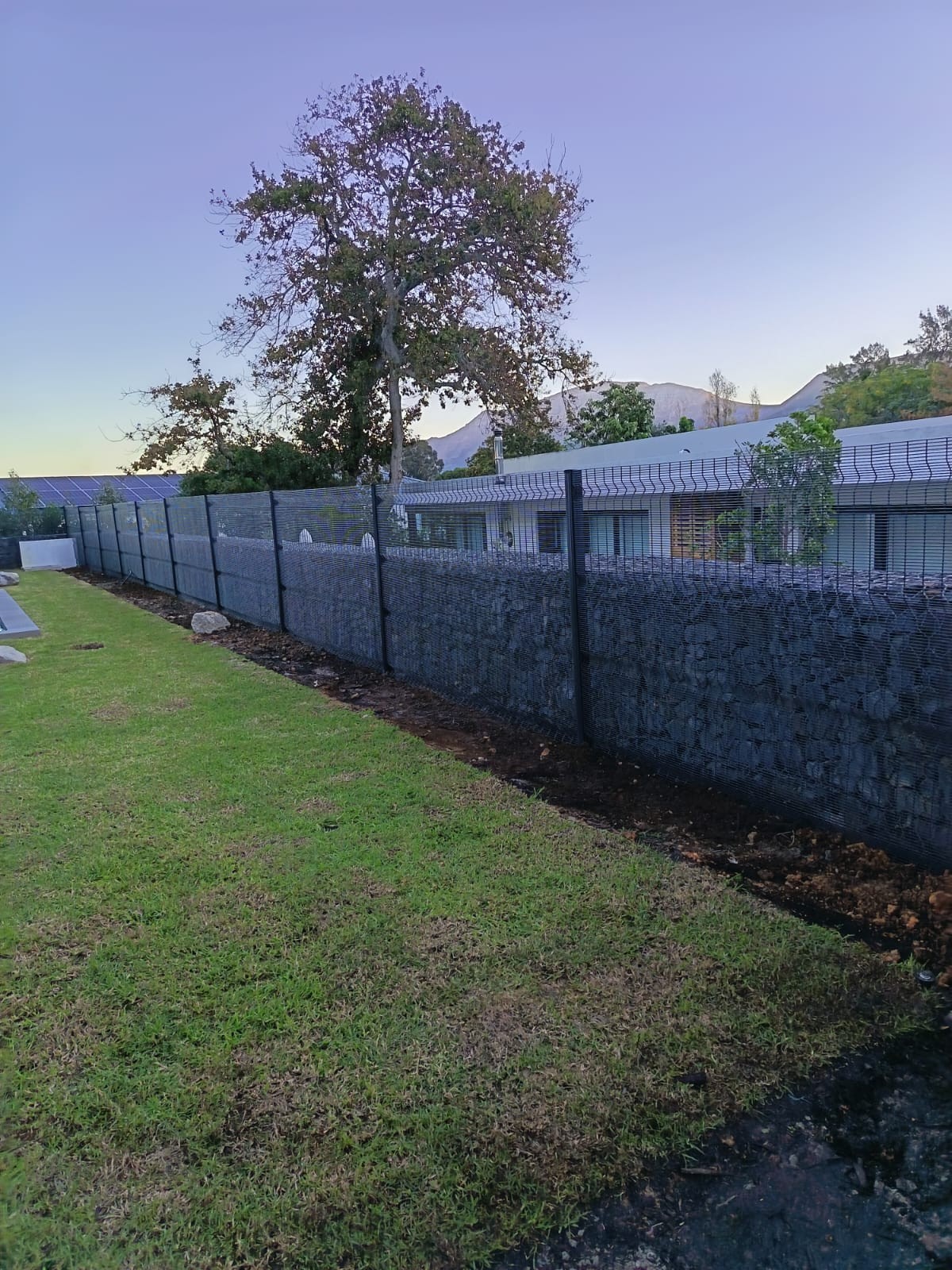 Stone-filled gabion wall with black wire mesh fence on top