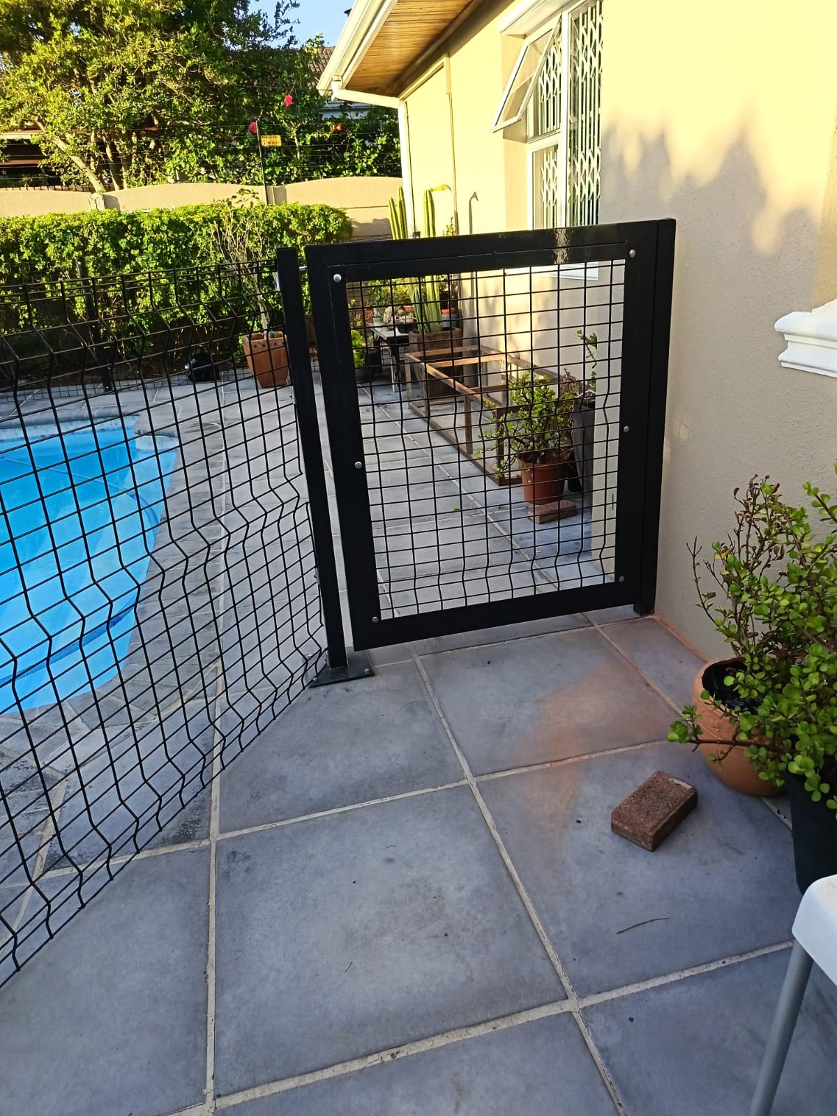 Black metal gate and matching wire fence beside a pool
