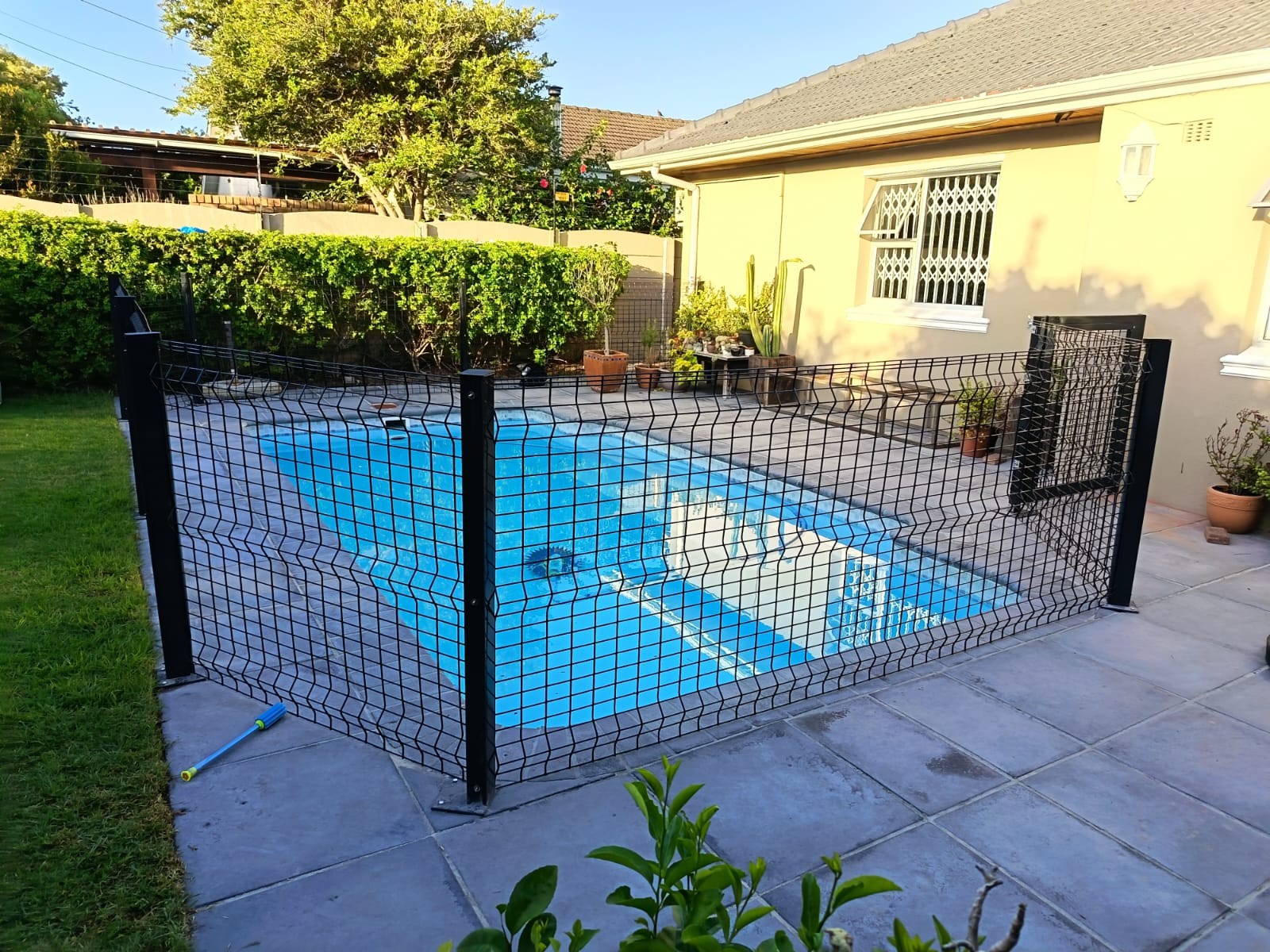 Black wire mesh pool safety fence around a swimming pool