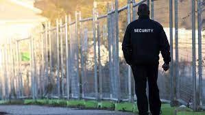 Uniformed security guard patrolling along a perimeter fence