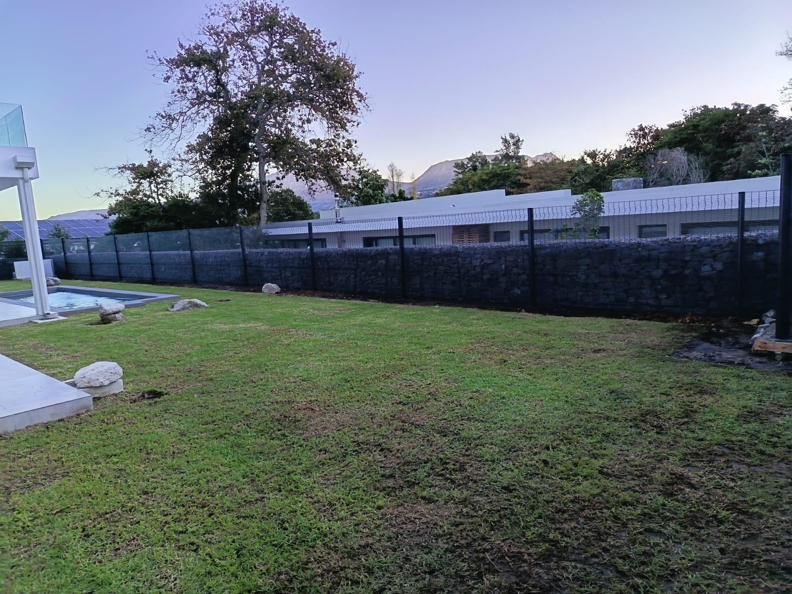 Gabion wall topped with black wire fence beside a pool