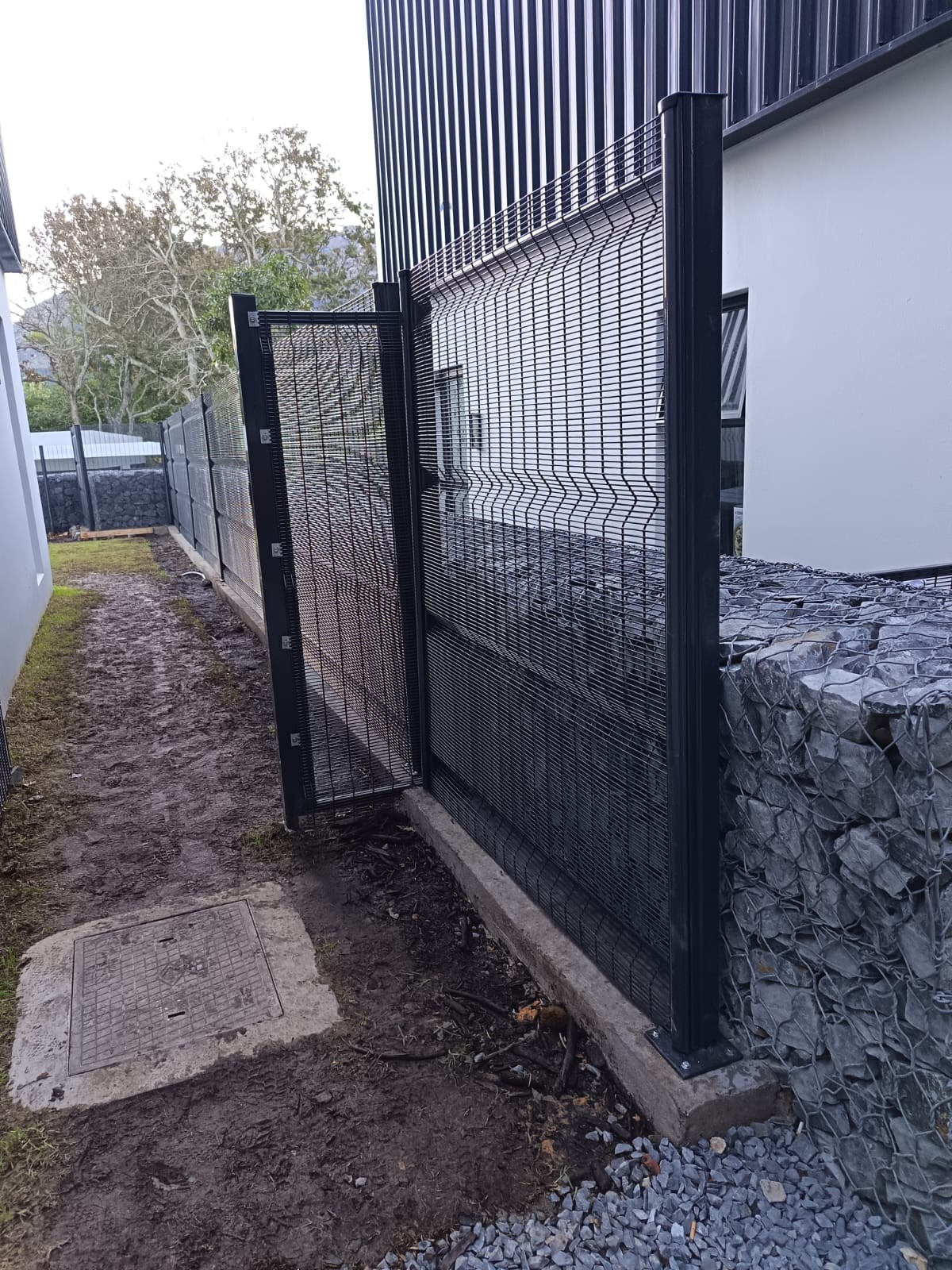 Black metal mesh security fence alongside a gabion wall