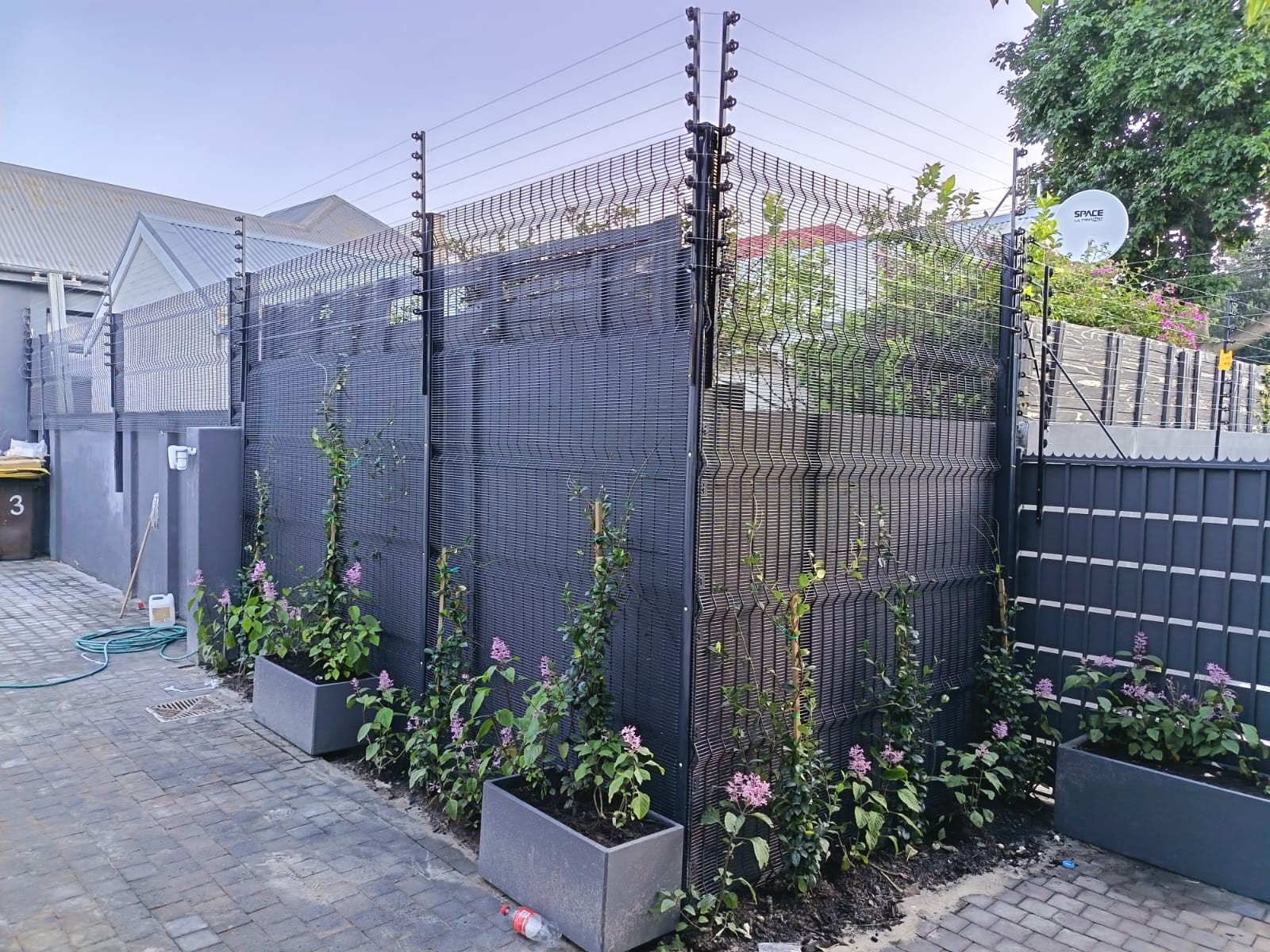 Dark grey metal mesh fence topped with electric security wires